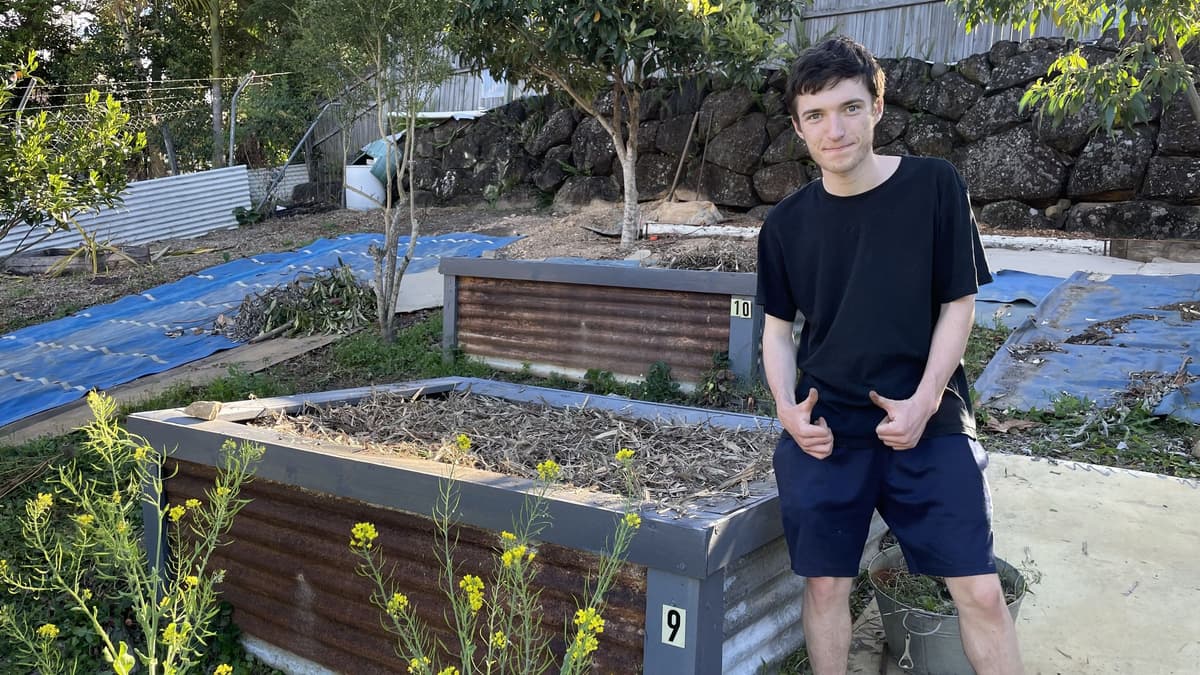 A young gardener giving two thumbs up beside newly built corrugated raised beds