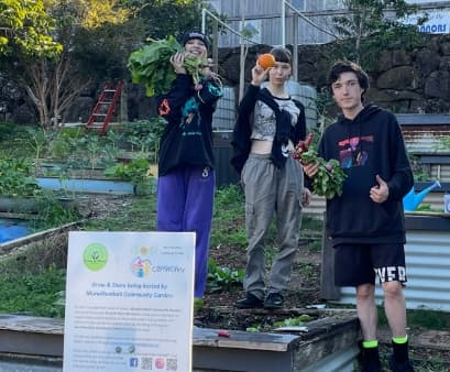 Three young people showing off their harvest at the community garden