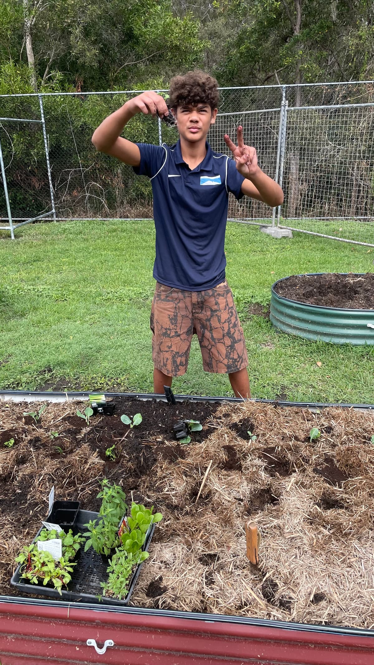 A student flashing a peace sign over a raised bed they have just planted