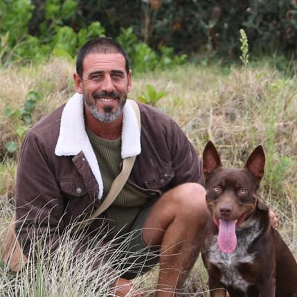 Seb crouched in the dune grass with his brown kelpie
