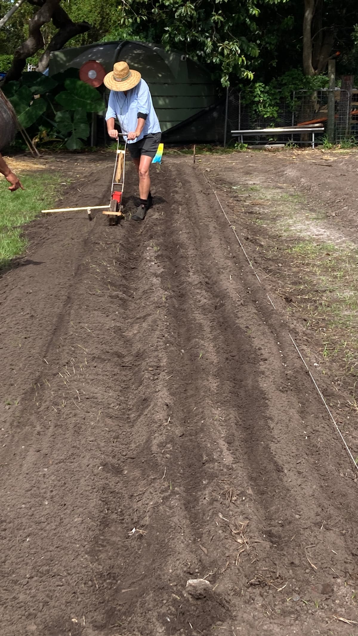 Seb in a straw hat working a hand plough along a new bed