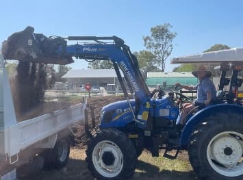 A front-end loader tipping compost into a trailer at the farm