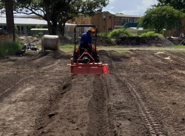 A compact tractor working bare ground into beds at the school